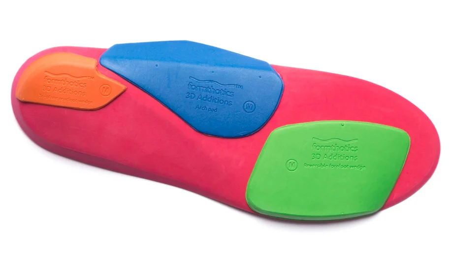 Underside of a Formthotics orthosis showing a blue longitudinal arch pad beneath the arch and a green reversible wedge beneath the forefoot